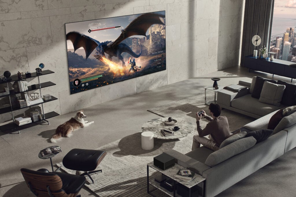 Lifestyle image of a man playing a video game on a wall-mounted LG Signature OLED M3 TV with LG Zero Connect technology