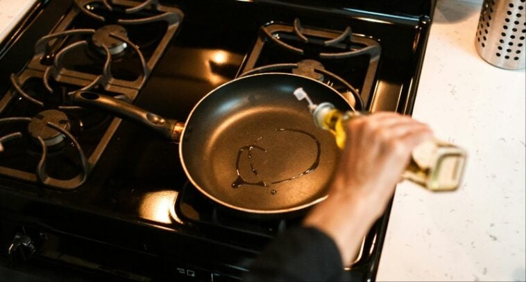Cooking oil being poured into a black non-stick pan resting on a stovetop burner | ©Image Credit: Pexels / RDNE Stock project
