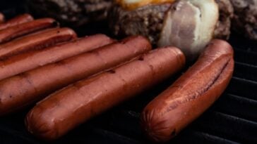 A close-up of hot dogs cooking on a grill | ©Image Credit: Unsplash / Oliver Fetter