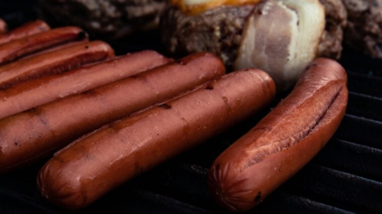 A close-up of hot dogs cooking on a grill | ©Image Credit: Unsplash / Oliver Fetter