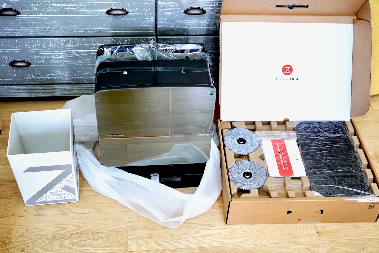 Unboxing scene showing Roborock docking station with accessories, mop pads, and setup materials 