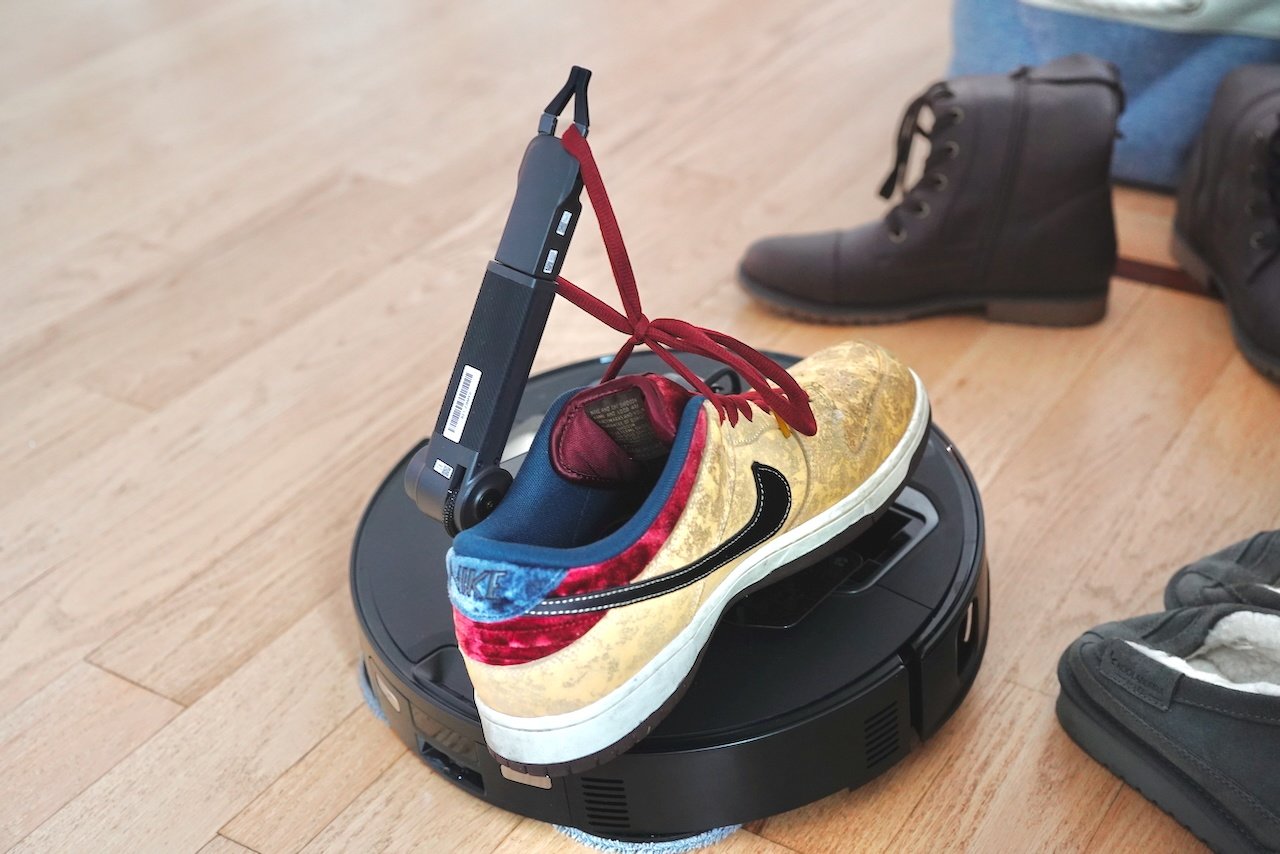 Roborock Saros Z70's robotic arm lifting a high-top sneaker while surrounded by other shoes on wooden floor 