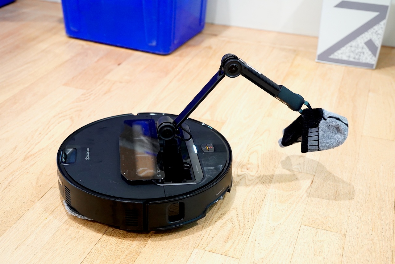 Roborock Saros Z70 with OmniGrip robotic arm fully extended, gripping a sock while positioned on wooden floor