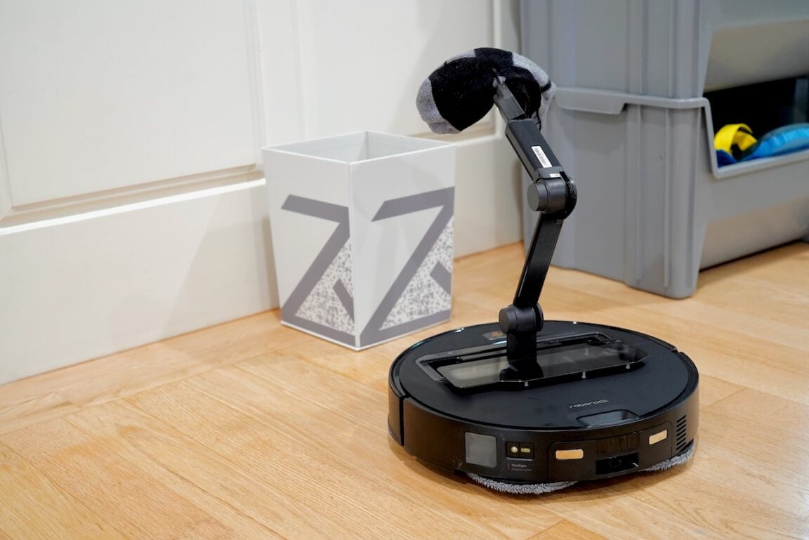 Roborock Saros Z70 with extended robotic arm gripping a sock, demonstrating the OmniGrip functionality | ©Image Credit: GEEKSPIN