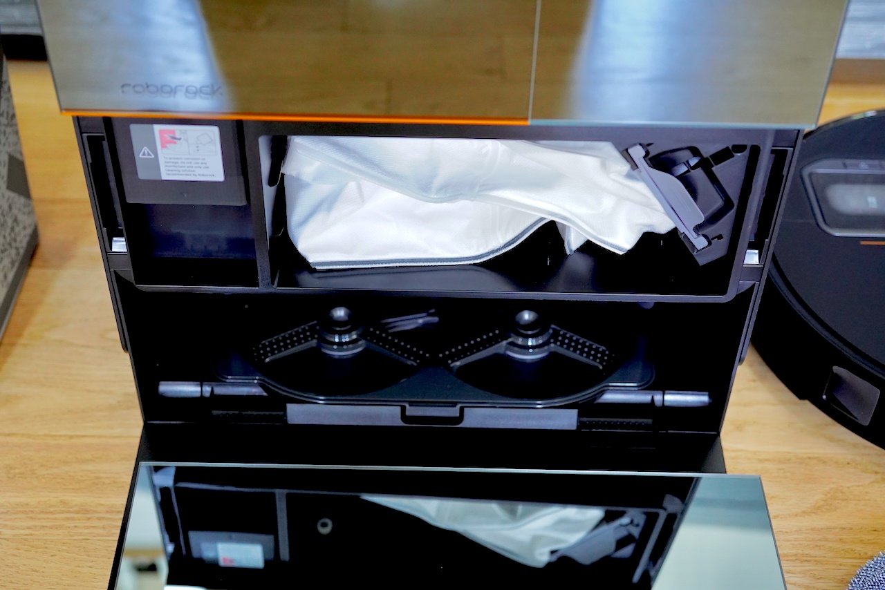Interior view of Roborock Multifunctional Dock 4.0 with compartments open showing automated mop washing system with rotating cleaning brushes, water reservoirs, and maintenance components