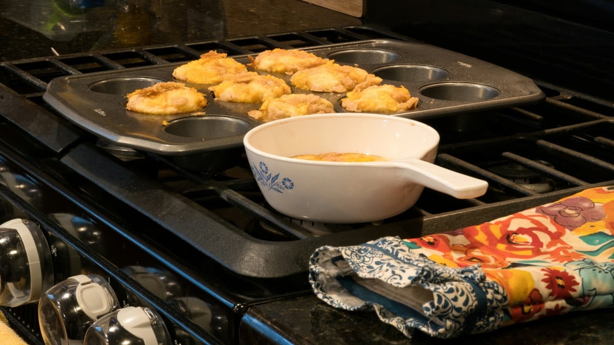 Peach muffins on the stove with a pair of oven mitts next to it