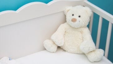 A white teddy bear sitting inside a baby's crib against a blue wall | ©Image Credit: Pixnio