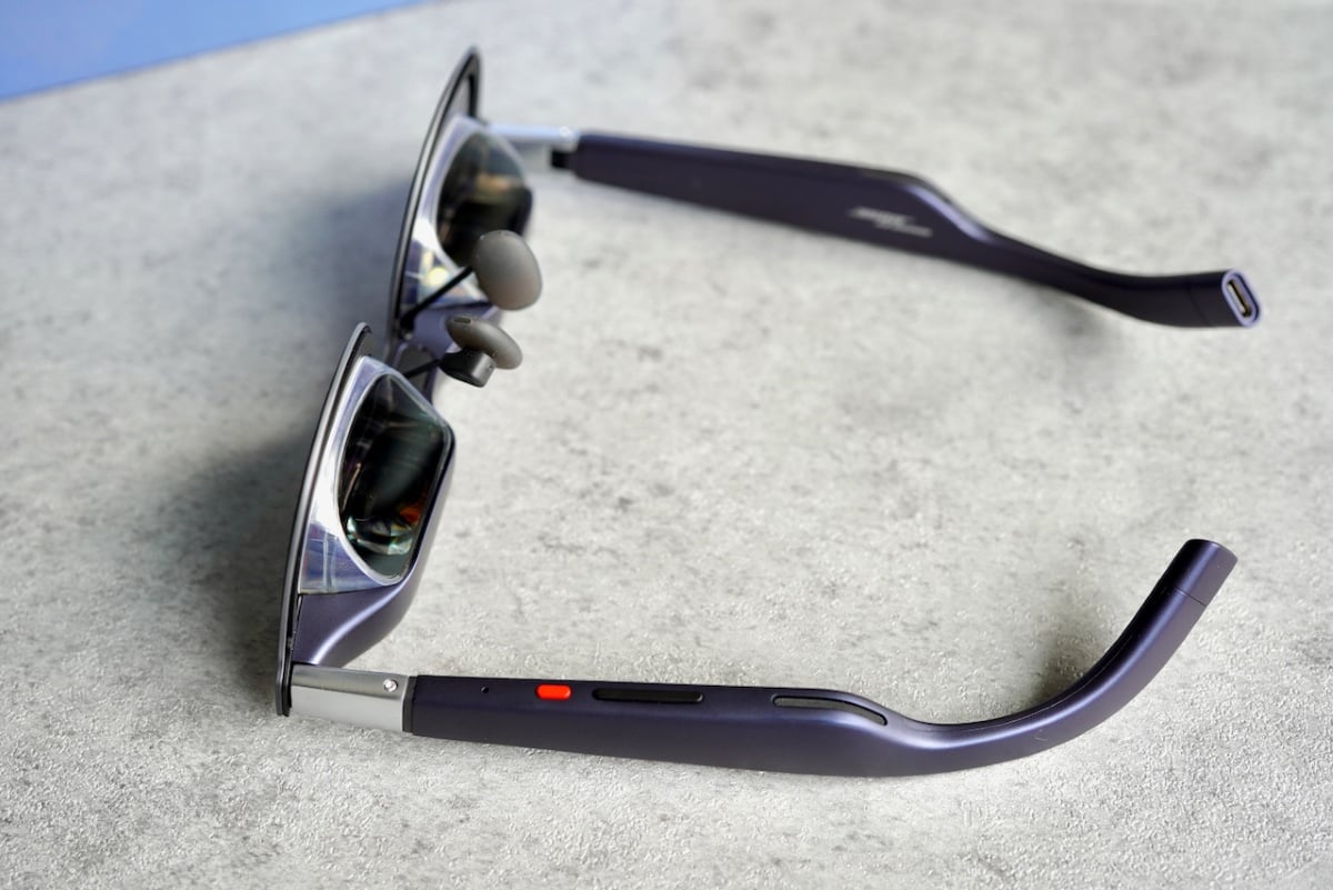 Close-up side view of the XREAL 1S glasses highlighting the physical controls on the temple, including the red button and tactile areas