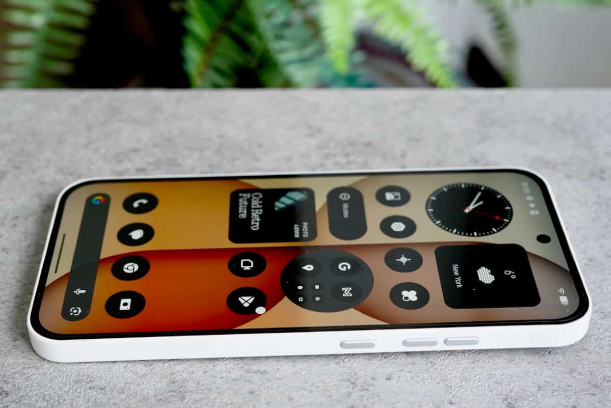 The Nothing Phone (4a) lying flat, displaying the colorful home screen with Nothing OS widgets and a punch-hole camera.