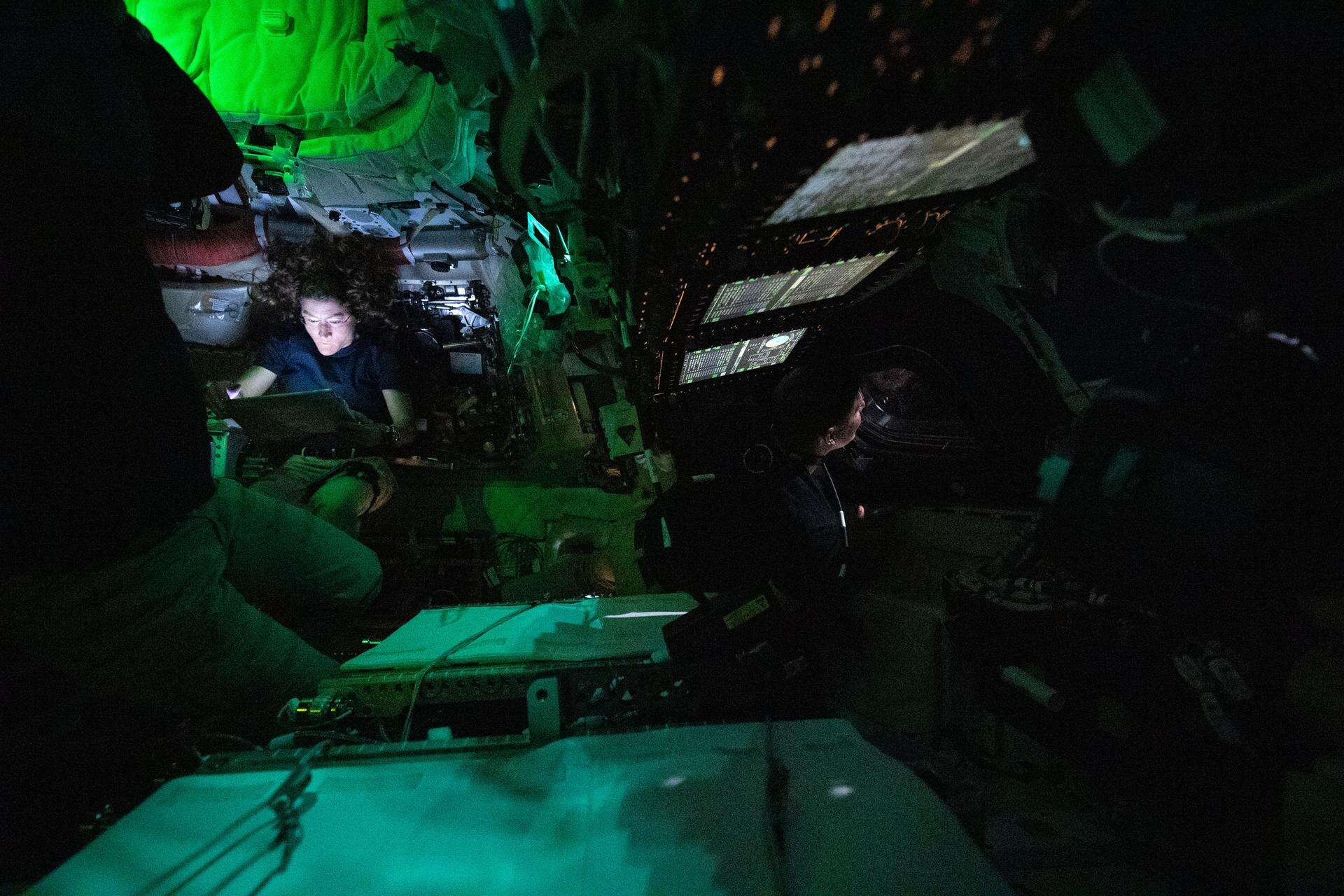NASA astronaut Christina Koch is illuminated by a screen inside the darkened Orion spacecraft on the third day of the agency's Artemis II mission. To the right of the image's center, CSA astronaut Jeremy Hansen is seen in profile peering out of one of Orion's windows. Lights are turned off to avoid glare on the windows. | ©Image Credit: NASA
