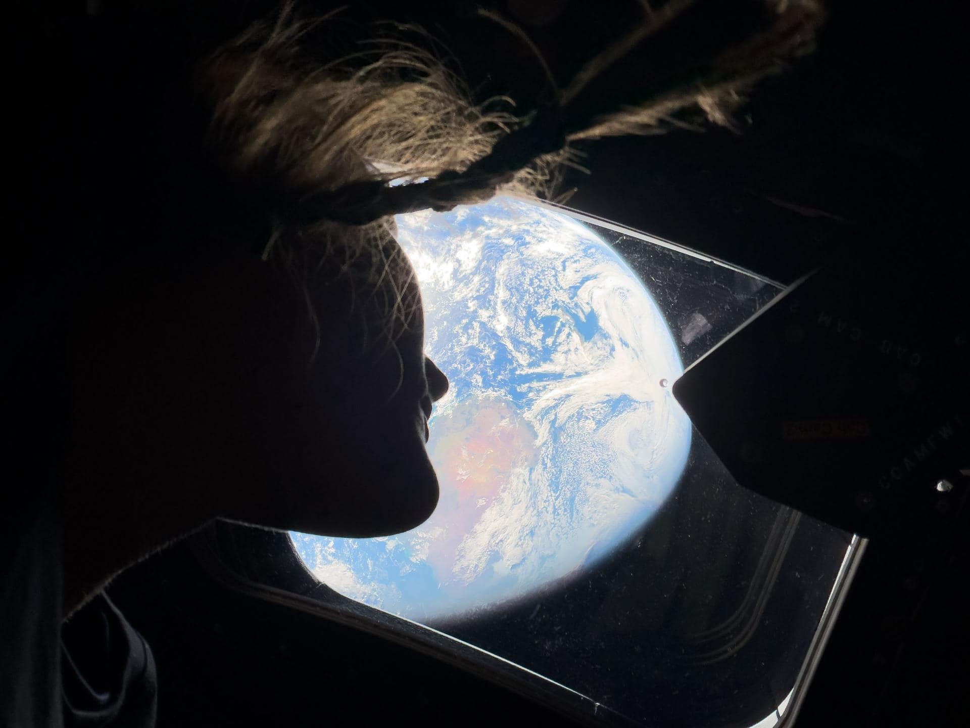 NASA astronaut and Artemis II mission specialist Christina Koch peers out of one of the Orion spacecraft's main cabin windows, looking back at Earth, as the crew travels towards the Moon. | ©Image Credit: NASA