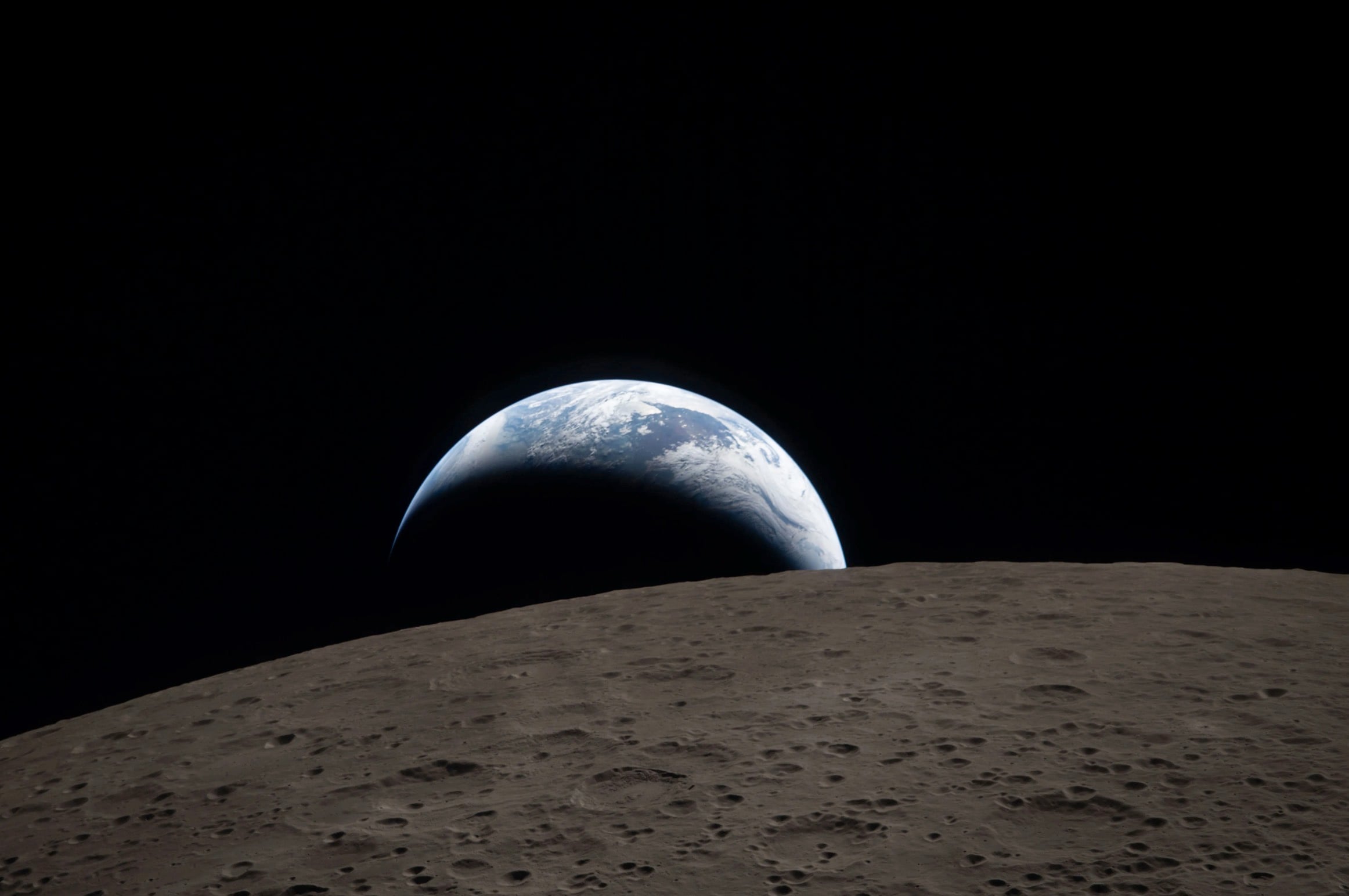 At 6:41 p.m. EDT on April 6, 2026, the Artemis II crew documented a stunning Earthset from their Orion spacecraft. The image shows our muted blue planet, streaked with bright clouds, dipping behind the Moon’s jagged horizon. While one side of Earth is shrouded in night, the sunlit side displays weather patterns over Australia and Oceania.  In the lunar foreground, the Ohm crater is prominently featured. This complex crater boasts terraced walls and a flat interior marked by central peaks—geological features created when the lunar crust briefly liquefied and splashed upward during a massive impact. ©Image Credit: NASA