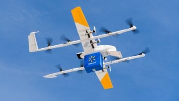 Wing’s autonomous drone, equipped with a Walmart delivery box, flies over a clear sky | ©Image Credit: Wing