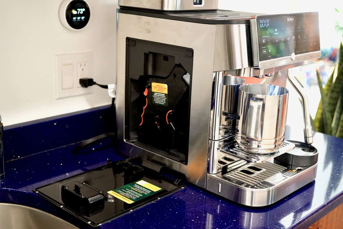 Side panel of the Ninja AutoBarista Pro opened to show the internal brew group mechanism and cleaning instructions label.